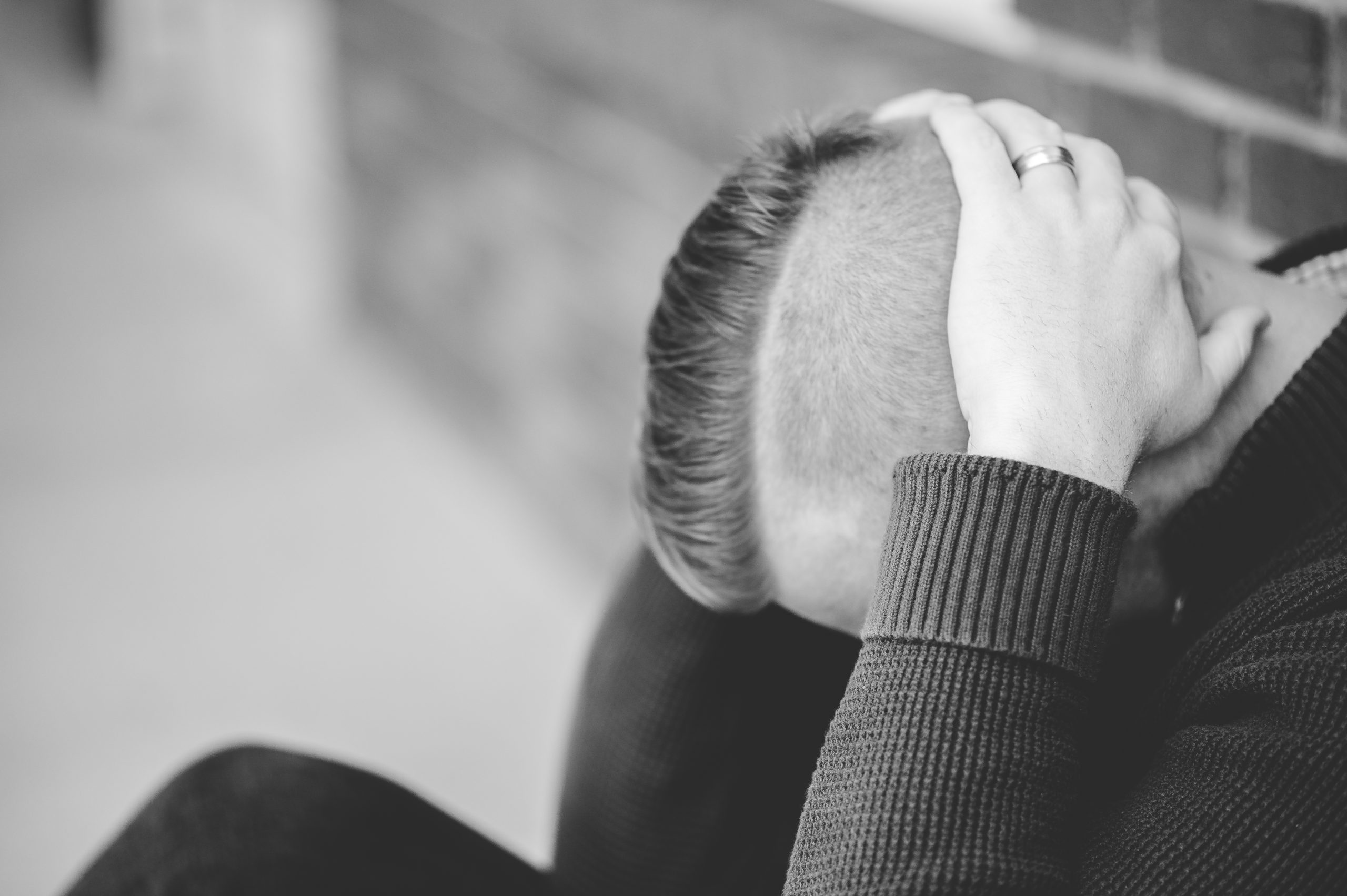 grayscale-shot-male-sitting-down-ground-while-holding-his-head